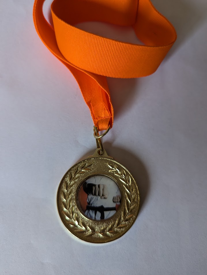 Gold medal with image of a punching karateka. It has an orange ribbon.